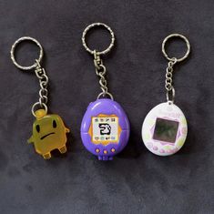 three key chains with different designs and colors on them, one has an alarm clock in the shape of a frog