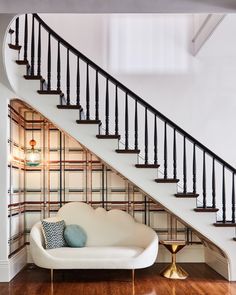 a white couch sitting under a stair case in a living room next to a wooden floor