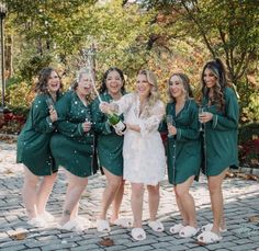 a group of women standing next to each other in green dresses holding champagne bottles and flutes