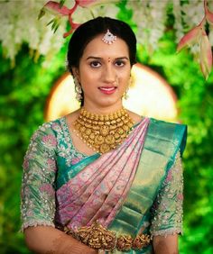 a woman in a green and pink sari with gold jewelry on her neck is smiling at the camera