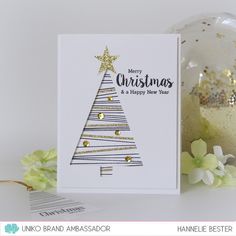 a card with a christmas tree on it next to a glass ornament and flowers