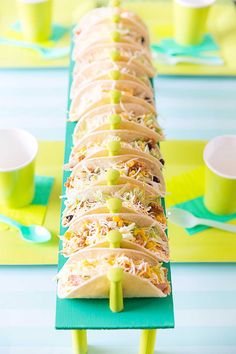 there are many tacos lined up on the long table with cups and spoons