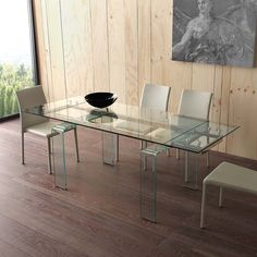 a glass dining table with white chairs in front of a large painting on the wall