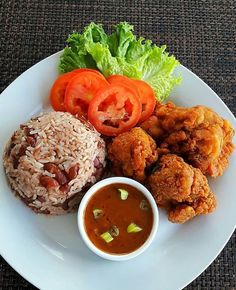 a white plate topped with rice, meat and veggies next to a bowl of sauce