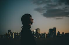 a woman standing in front of a city skyline at night with her head turned to the side