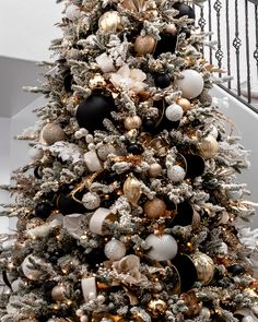 a decorated christmas tree with black and gold ornaments on it's branches, in front of a staircase