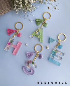 four different key chains with letters and tassels hanging from them on a blue surface