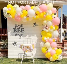 a white chair sitting in front of a building with balloons on the wall and a sign that says first bee day