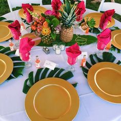 the table is set with pineapples, pink and orange flowers, gold plates, and tropical leaves