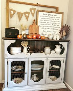 a white hutch filled with dishes and pumpkins next to a sign that says give