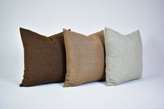 three different colored pillows sitting side by side on a white surface, one is brown and the other is tan