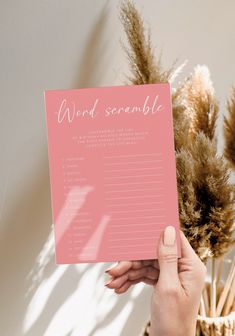 a person holding up a pink card with the word and scramble on it in front of some dried plants