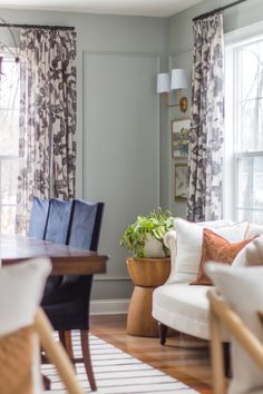 a living room filled with furniture and a wooden table in front of two large windows