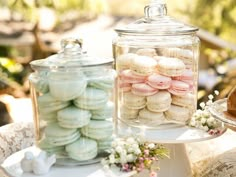 two glass jars filled with macaroons on top of a white table covered in flowers