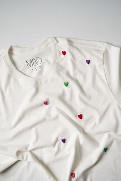 a white t - shirt with colorful hearts on the front and back, sitting on top of a table