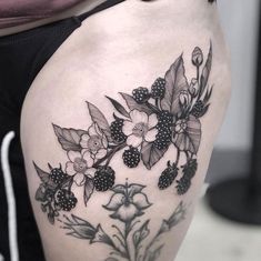 a woman's thigh with blackberries and flowers on the bottom part of her leg