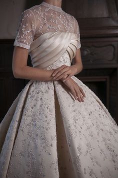 a woman in a white dress standing next to a fireplace with her hands on her hips