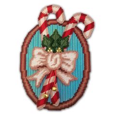 a cross stitch ornament with candy canes and holly on the top, in front of a blue background