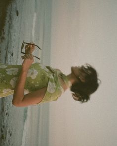 a woman standing next to the ocean holding an object in her hand and looking up