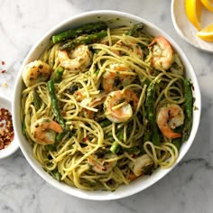 a bowl of pasta with shrimp and asparagus next to lemon wedges on a marble table