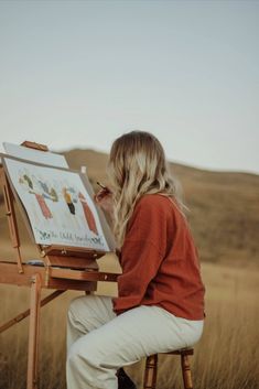 a woman sitting in front of an easel painting