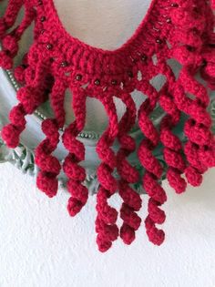 a red crocheted scarf hanging on a white wall