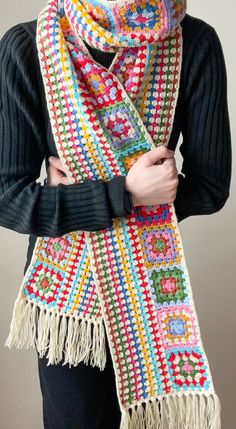 a woman wearing a multicolored crocheted scarf with fringes on it