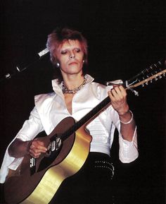 a woman holding a guitar while standing in front of a microphone and wearing a white shirt