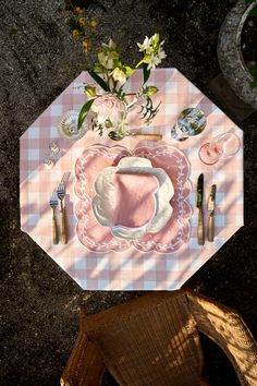 an overhead view of a table setting with pink and white checkered cloth, silverware and flowers