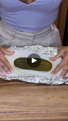 a woman is holding some tin foil with her hands on the top of an oval shaped pickle