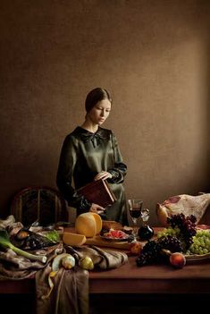 a woman standing in front of a table filled with fruit and vegetables next to a window