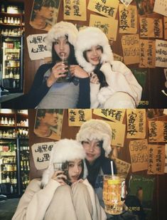 two people wearing hats and holding drinks in front of a wall covered with signs that spell out chinese characters