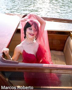 a woman in a red dress is sitting in a boat with a veil over her head