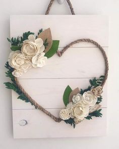 a heart shaped sign with flowers and leaves hanging on a rope hanger in the shape of a heart