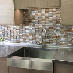 a stainless steel sink in a kitchen with wooden cabinets and tile backsplashing