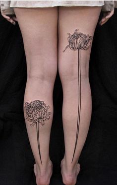 two women's legs with tattoos on them, one has flowers and the other has leaves