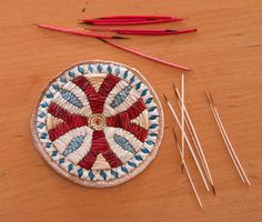 a wooden table topped with different types of knitting needles and an embroidered pincust