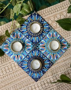 three white candles sitting on top of a blue and white plate next to green leaves