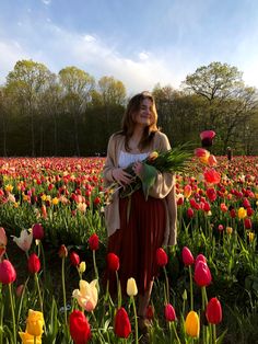 a woman standing in a field full of tulips holding a bunch of flowers