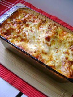 a casserole dish with cheese and meat in it sitting on a wooden cutting board