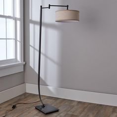 a floor lamp with a shade on it in front of a white wall and wooden floor