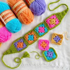 crocheted items are displayed on a white tablecloth with orange, pink, and blue balls of yarn