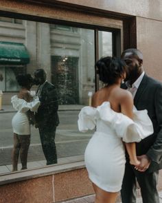 a man and woman standing in front of a store window looking at each other's reflection