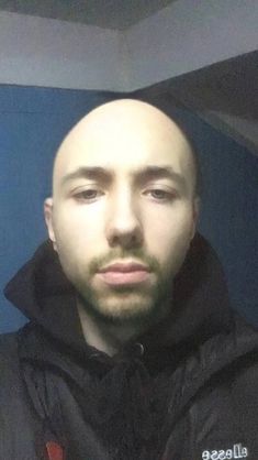 a bald man wearing a black hoodie and looking at the camera with an intense look on his face