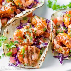 three tacos with shrimp and coleslaw on them sitting on a white plate