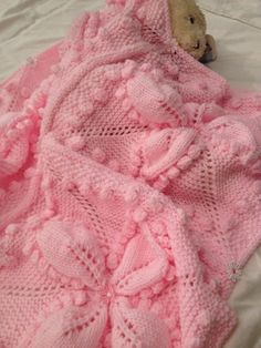 a teddy bear is wrapped up in a pink crocheted blanket on a bed