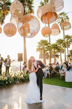 a bride and groom share their first dance under hanging lights at the beach wedding reception