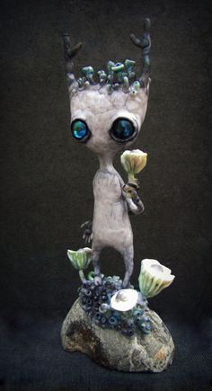 an alien figurine with blue eyes is holding two flowers in his hand and standing on top of a rock