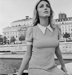 black and white photograph of a woman sitting on the edge of a pier with buildings in the background