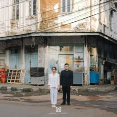 a man and woman standing in front of an old building on a street corner with power lines above them